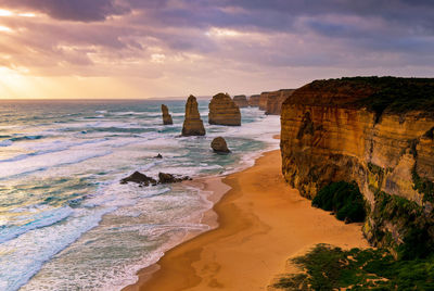 Scenic view of cliff at beach against cloudy sky during sunset