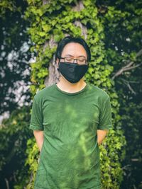 Young man in green t- shirt against green plants and trees.