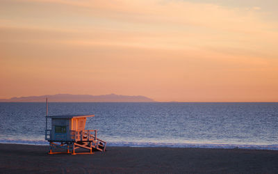 Lifeguard hut at beach against sky during sunset