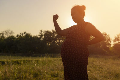 Pregnant woman standing in the meadow warm tones.