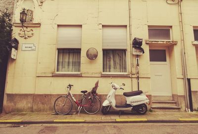 Bicycle and motor scooter parked by building