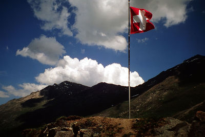 Low angle view of switzerland flag on mountain against cloudy sky