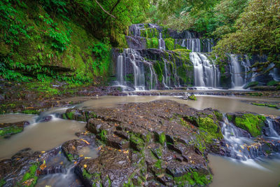 Waterfall by trees against sky