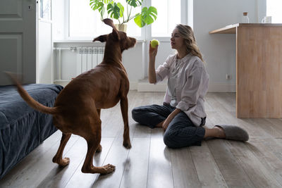 Full length of woman playing with ball while sitting on floor at home