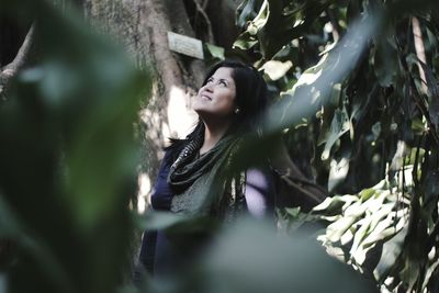 Close-up of smiling young woman against tree trunk