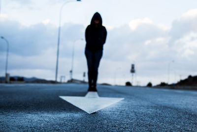 Man standing on arrow marking over road against sky