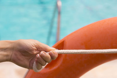 Cropped hand of woman holding life belt rope against swimming pool