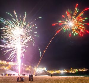 Firework display over sea against sky at night