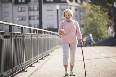 Senior woman walking on footbridge, using walking stick