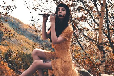 Hipster woman playing flute while sitting on rock