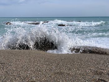 Waves splashing on shore at beach against sky