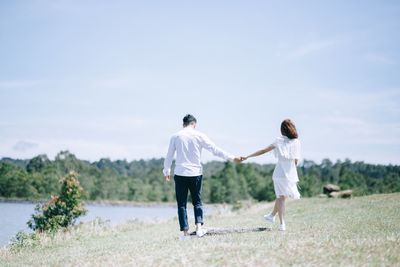 Rear view of couple walking on grassy field against sky