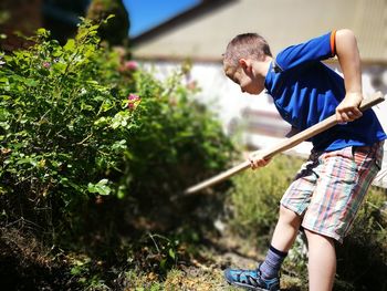 Low angle view of boy holding stick while standing on field at back yard