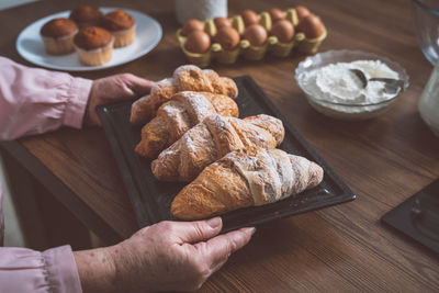 Cropped hand of senior woman holding croissant in tray