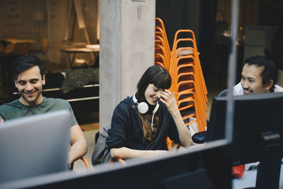 Happy female computer programmer sitting with male colleagues in office