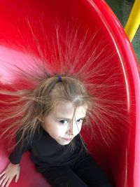 Cute girl with tousled hair sitting in slide at park