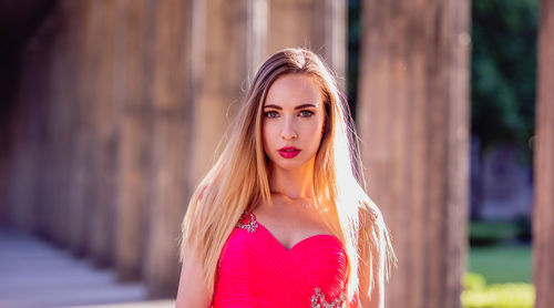 Close-up portrait of beautiful young woman in pink evening dress at colonnade