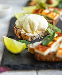 Sandwiches with tartine bread, poached egg, avocado and grilled cheese with salad leaves and lime