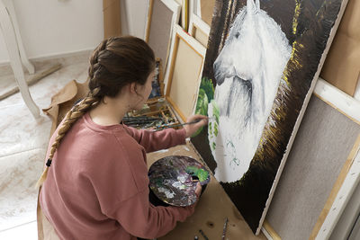 High angle view of teenage girl painting horse on canvas at home