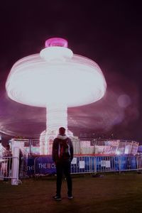 Rear view of man standing in illuminated amusement park at night