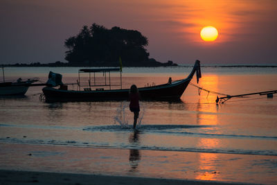 Silhouette people on sea against sky during sunset