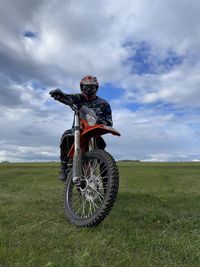 Low section of man riding bicycle on field against sky