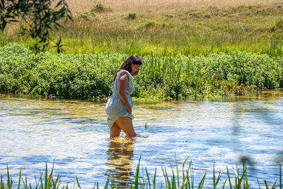 Girl wearing sundress, walking knee deep in creek on a hot day in summer