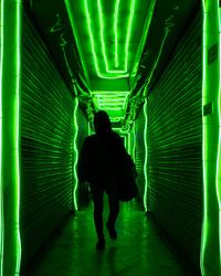 Rear view of man walking in illuminated corridor