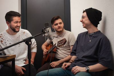 Three men record song, play guitar, communicate and smile. recording studio.