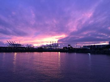 Illuminated city by sea against sky at sunset