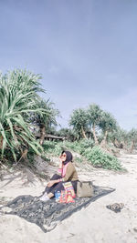 Rear view of woman sitting on beach against sky