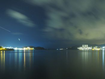 Illuminated cityscape by sea against sky at night