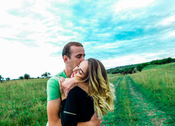 Happy couple standing on field against sky