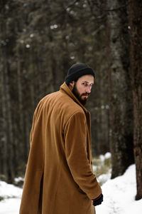 Young man wearing hat standing in forest during winter