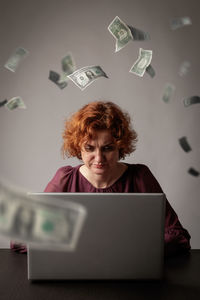Paper currencies falling on mature woman using laptop over desk