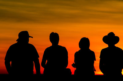 Silhouette friends sitting on bench against sky during sunset