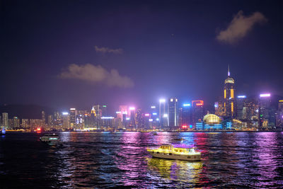 Illuminated buildings by sea against sky at night