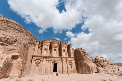 Low angle view of the monastery at petra in jordan against a blue sky with clouds