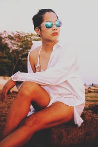 Seductive woman sitting on rock at beach against sky during sunset