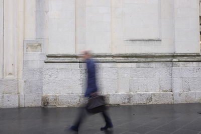 Blurred motion of man walking against wall