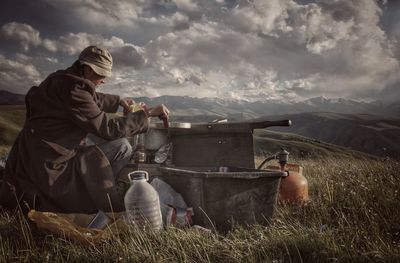 Man cooking food on field against sky during camping