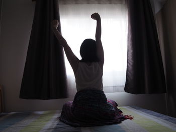 Rear view of woman standing by window at home