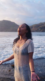 Young woman looking away while standing on beach against sky