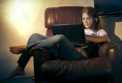 Cute girl using laptop sitting on sofa at home