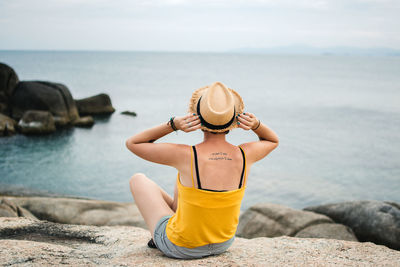 Rear view of man sitting on rock by sea