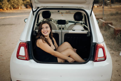 Woman looking away while sitting in car trunk