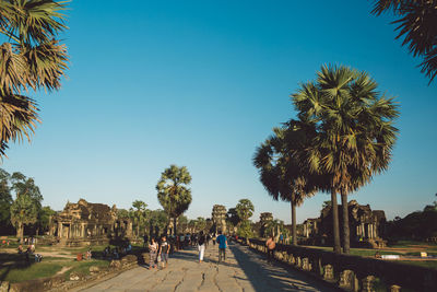 People on footpath amidst trees at angkor wat against sky