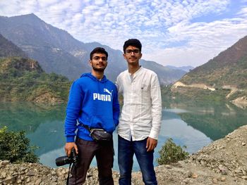 Portrait of friends standing on mountain by lake against cloudy sky