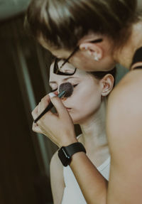 A young makeup artist applies powder with a brush to a girl s eyes.