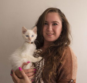 Portrait of young woman with cat standing against white background